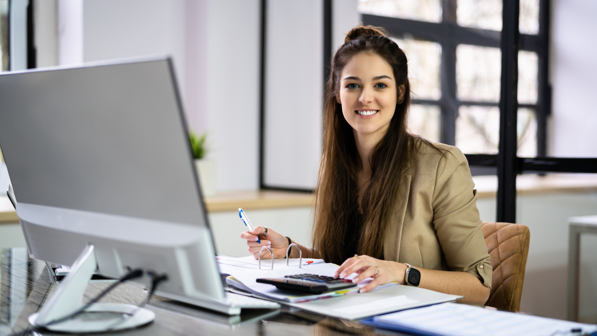 A bookkeeper sat at a desk with a computer inputting data from business records